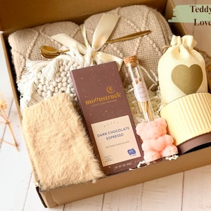 May include: A brown gift box with a beige blanket, a chocolate bar, a small mug, a teddy bear, and a bag with a heart on it. The box is labeled "Teddy Bear Love Box".