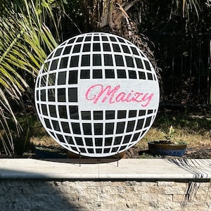 May include: A black and white disco ball with a pink glitter name "Maizy" on it.