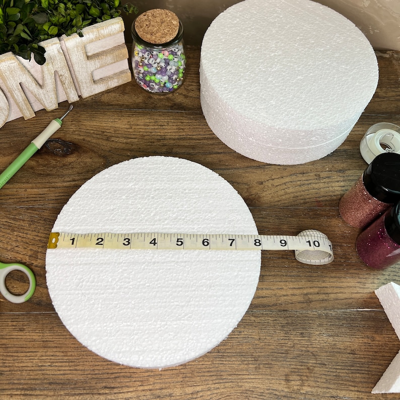 May include: Two white round foam cake dummies, one measuring 8 inches in diameter and the other measuring 10 inches in diameter. The smaller cake dummy is being measured with a tape measure.