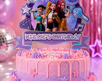 May include: A multi-layered purple and blue cake topper featuring three pop star figures, a disco ball, a number 6, and the text "KHLOE'S BIRTHDAY" and "HUNTRX". The topper is displayed on a round cake with pink and purple frosting, drips, and sprinkles.