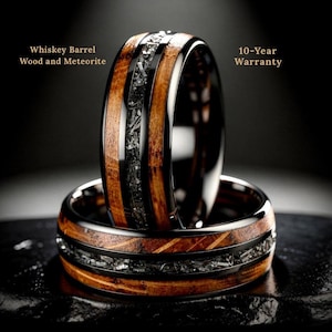 May include: Two rings with a whiskey barrel wood and meteorite design. The rings have a black band with a wood grain pattern and a center of dark gray meteorite. The text "Whiskey Barrel Wood and Meteorite" and "10-Year Warranty" are visible.