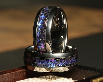 May include: Two black tungsten carbide rings with a blue and purple glitter inlay. The rings are stacked on top of each other and are in a wooden box.