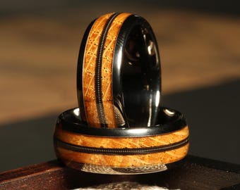 May include: Two black tungsten carbide rings with a wood inlay. The rings have a black band with a thin black line running around the wood inlay. The wood inlay is a light brown color.