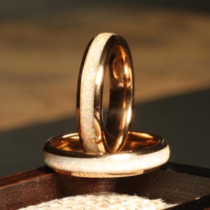 May include: Two gold wedding bands with a white opal inlay. The bands are stacked on top of each other.