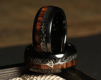 May include: Two black rings with a wood inlay. The rings have a black metal finish and a wood inlay with a natural wood grain pattern. The rings are stacked on top of each other.
