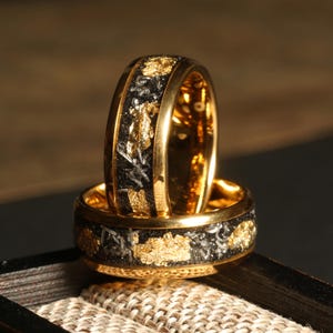 May include: Two gold rings with black and gold inlay. The rings are stacked on top of each other.