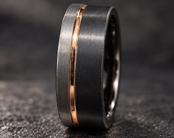 Op de afbeelding: Een brede ring met een donkergrijze geborstelde metalen afwerking en een enkele, gepolijste roségoudkleurige inleg die verticaal rond het midden van de band loopt, wat zorgt voor een duidelijk contrast tussen de matte en glanzende oppervlakken.