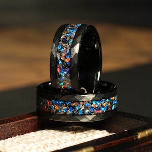 Könnte beinhalten: Zwei schwarze Ringe aus Wolframcarbid mit einem Band aus schimmerndem blauem, grünem und rotem Glitzer. Die Ringe sind übereinander gestapelt.