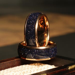 May include: Two gold rings with a dark blue speckled finish. The rings are stacked on top of each other.