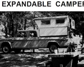 May include: A black and white photo of a vintage pickup truck with a pop-up camper attached to the bed. The truck is parked in a wooded area with trees in the background. The camper has two windows and a door. The truck has a wooden picnic table in front of it.