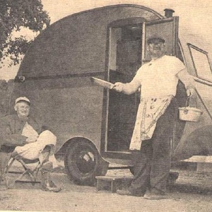 Könnte beinhalten: Zwei Personen stehen vor einem Vintage-Wohnwagen in Silber, der die Form einer Träne hat. Eine Person hält eine Bratpfanne und die andere sitzt auf einem Klappstuhl.