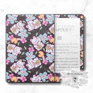 May include: A black and white Kindle Paperwhite e-reader with a custom cover featuring a repeating pattern of white cats holding gold coins and pink, blue, and yellow flowers on a black background. The text "Happy go lucky" is printed on the cover. The text "Chapter 1" is visible on the screen.