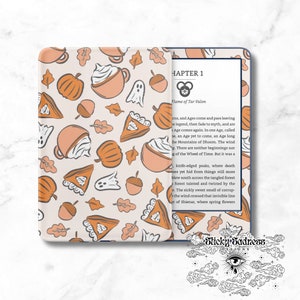 May include: A beige Kindle case with a fall-themed pattern featuring pumpkins, pie slices, coffee cups, acorns, leaves, and ghosts. The Kindle is open to a page with text from "Flame of Tar Valon". The case is from Sticky Sadness.