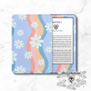 May include: A blue and pink Kindle e-reader cover with a white daisy pattern. The cover has a rainbow design with a white border. The screen displays the text "Chapter 1 Flame of Tar Valon".