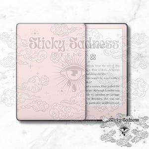 May include: A pink e-reader with a white and gray design featuring clouds and a stylized eye with a teardrop. The text "Sticky Sadness" is on the cover. The e-reader is open to a page with text.