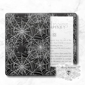 Peut inclure: Une housse pour liseuse Kindle avec un motif d'araignée noir et blanc. Le texte "Sticky Sadness" est visible sur l'écran.