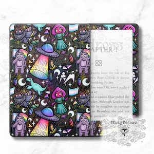 Peut inclure: Une liseuse Kindle Paperwhite noire et verte avec une coque illustrée colorée représentant une variété de personnages fantastiques, notamment des extraterrestres, des fantômes et des créatures mythologiques. La coque présente un motif répétitif de drapeaux arc-en-ciel, d'étoiles, de lunes et de cristaux. Le texte "Your Existence Matters" est présenté sur la coque.