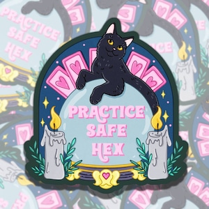 Puede incluir: Un gato negro se sienta sobre una bola de cristal con el texto "PRACTICE SAFE HEX" en su interior. El gato está rodeado de cartas de tarot rosas y dos velas blancas con llamas. El fondo es azul oscuro con estrellas.