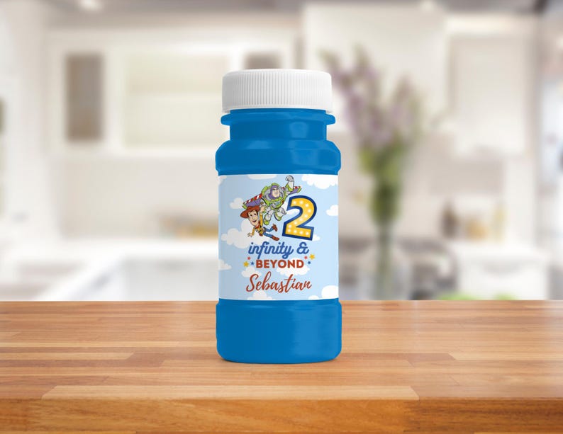 Op de afbeelding: Een blauwe bellenblaasfles met een witte dop. Het etiket toont personages uit een populaire animatiefilm, het nummer 2, de tekst "infinity & beyond" en een naam. De fles staat op een houten oppervlak.
