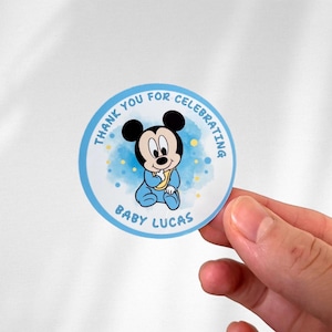 May include: Round blue and white thank you sticker with a cartoon baby Mickey Mouse wearing a blue onesie and a yellow bib. The sticker says "Thank you for celebrating Baby Lucas".