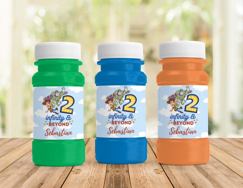 Op de afbeelding: Drie kleurrijke bellenblaasflessen: groen, blauw en oranje. Elke fles heeft een witte dop en een etiket met een cartoonafbeelding van Woody, Buzz Lightyear en het cijfer 2. De etiketten lezen ook "infinity & beyond" en een naam.
