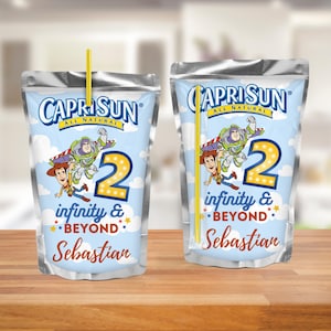 Puede incluir: Dos pouches de zumo Capri Sun con temática de Toy Story. Los pouches son azules y blancos con una imagen de Woody y Buzz Lightyear. El texto en los pouches dice "infinity & beyond" y "Sebastian".