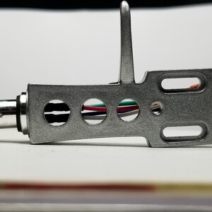 May include: Silver tone phono cartridge with a black, red, green, and white wire. The cartridge has a silver tone headshell with a small silver tone lever.