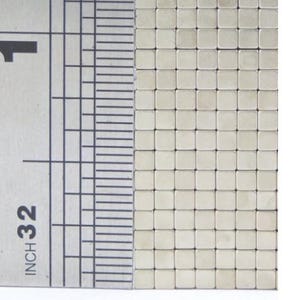 May include: Close-up of a collection of small, square, silver-colored magnets. A metal ruler with inch markings is positioned next to the magnets, showing the scale. The ruler reads "INCH 32".