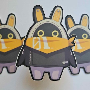 May include: Three black and white cartoon character stickers with yellow and white accents. The characters are wearing black jackets and yellow scarves. The characters have large eyes and bunny ears. The stickers are printed with the number "01" on the scarves.