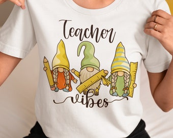 May include: White t-shirt featuring a design of three gnomes holding school supplies and the text "Teacher Vibes".