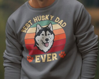 May include: A charcoal grey sweatshirt featuring a retro-style graphic of a husky dog. The graphic reads "Best Husky Dad Ever" with paw prints on either side of the text.