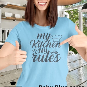Puede incluir: Una mujer lleva una camiseta azul claro con el texto "my kitchen my rules" en gris oscuro. La camiseta presenta un gorro de cocinero y un gráfico de batidor.