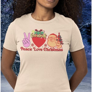 A woman wearing t-shirt with words Piece Love Christmas in Soft Cream Color