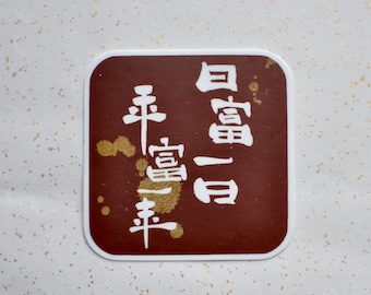May include: Square brown coaster with white border and Japanese text. The text is in a vertical format and is white. The background is white with small gold flecks.