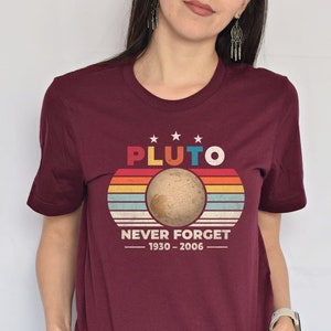 May include: Maroon t-shirt with a retro-style graphic of Pluto, the planet, with the text "Pluto Never Forget 1930-2006".