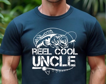 Puede incluir: Una camiseta azul marino con un gráfico blanco de un pez y el texto "Reel Cool Uncle".