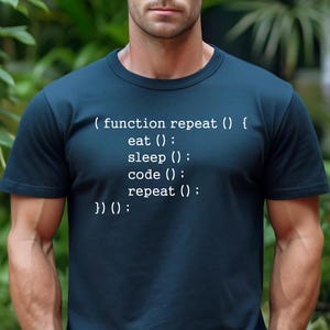 May include: Navy blue t-shirt with white text that reads "(function repeat () { eat (); sleep (); code (); repeat (); })() :". The word "NAVY" is printed in white at the bottom right corner. The shirt is a crew neck.