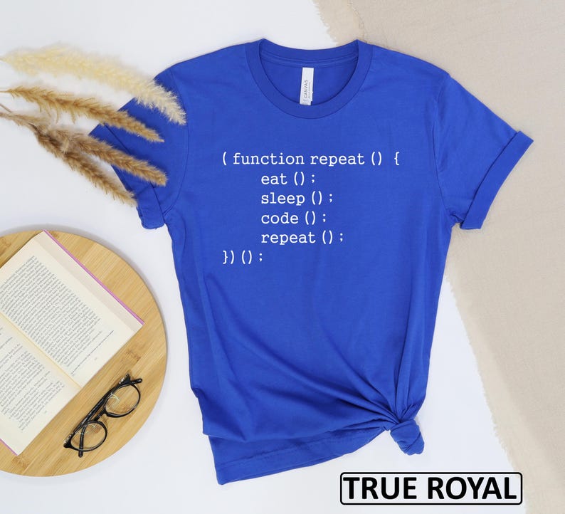 May include: Royal blue t-shirt with white text that reads "(function repeat () { eat (); sleep (); code (); repeat (); })() :". The shirt is folded at the bottom. The words "TRUE ROYAL" are in a black box at the bottom.