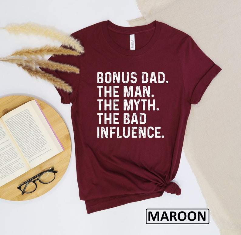 May include: Maroon t-shirt with white text that reads "Bonus Dad. The Man. The Myth. The Bad Influence."