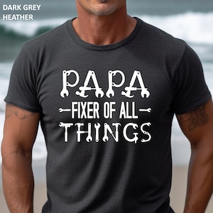 May include: Dark grey heather t-shirt with white text that reads "Papa - Fixer of All - Things" with wrench symbols surrounding the text.