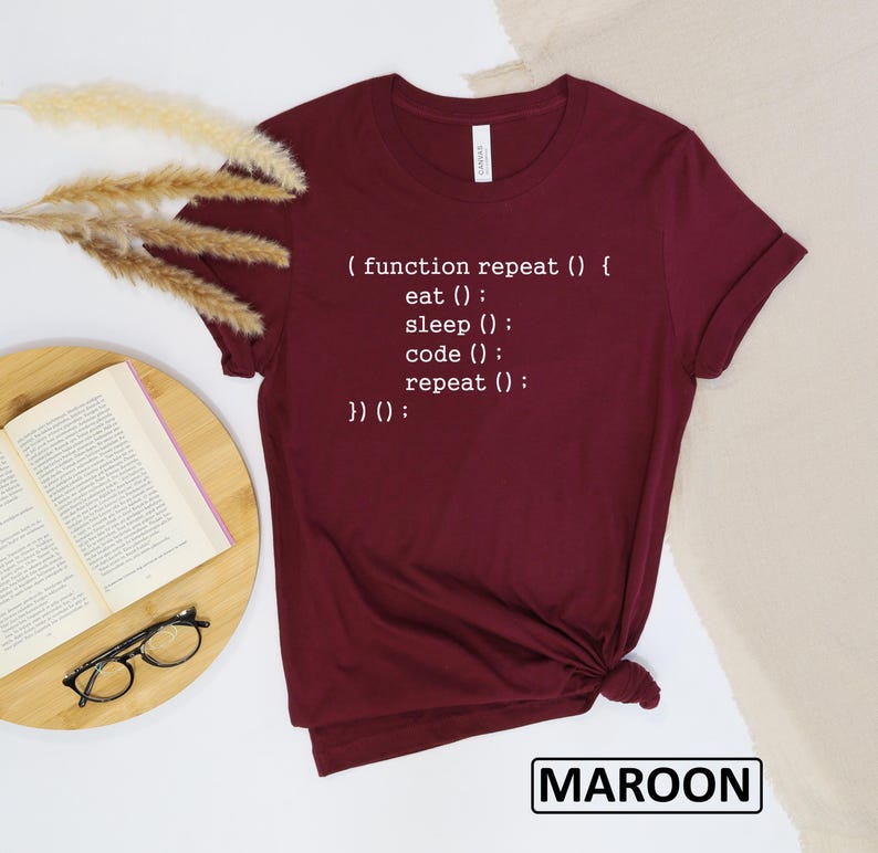 May include: Maroon t-shirt with white text that reads "(function repeat () { eat (); sleep (); code (); repeat (); })() :". The shirt is a solid color and has a crew neck. The word "MAROON" is printed in a white box at the bottom.