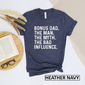 May include: Heather navy blue t-shirt with white text that reads "Bonus Dad. The Man. The Myth. The Bad Influence."