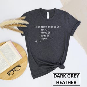 May include: Dark grey heather t-shirt with white text that reads "( function repeat () { eat (); sleep (); code (); repeat (); }) ();". The shirt also has a tag that says "Canvas". The words "DARK GREY HEATHER" are in a white rectangle.