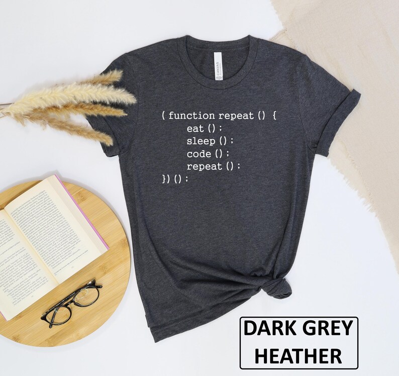 May include: Dark grey heather t-shirt with white text that reads "( function repeat () { eat (); sleep (); code (); repeat (); }) ();". The shirt also has a tag that says "Canvas". The words "DARK GREY HEATHER" are in a white rectangle.