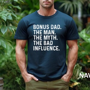 May include: A navy blue t-shirt with white text that reads "Bonus Dad. The Man. The Myth. The Bad Influence."