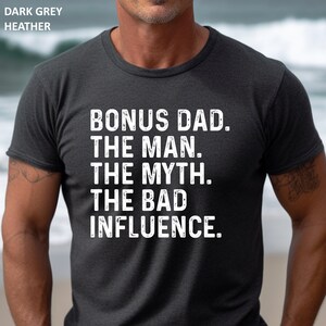May include: Dark heather grey t-shirt with the text "BONUS DAD. THE MAN. THE MYTH. THE BAD INFLUENCE."