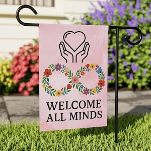 May include: A pink garden flag with the words "WELCOME ALL MINDS" in black. The flag features a heart symbol held by hands, and an infinity symbol made of colourful flowers. The flag is displayed on a black metal stand.