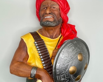 May include: A ceramic bust of a man wearing a red turban and a yellow vest. He is holding a silver shield with intricate designs and a sword.