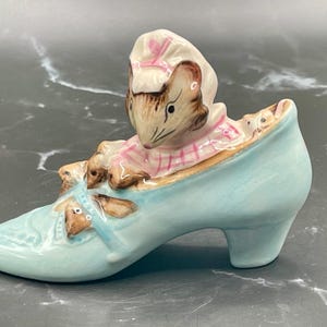 May include: A ceramic figurine of a mouse wearing a pink dress and hat, sitting inside a light blue shoe.