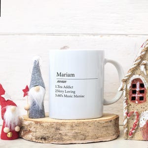 May include: White ceramic mug with a black design that says "Mariam noun 1.Tea Addict 2.Very Loving 3.60's Music Maniac"